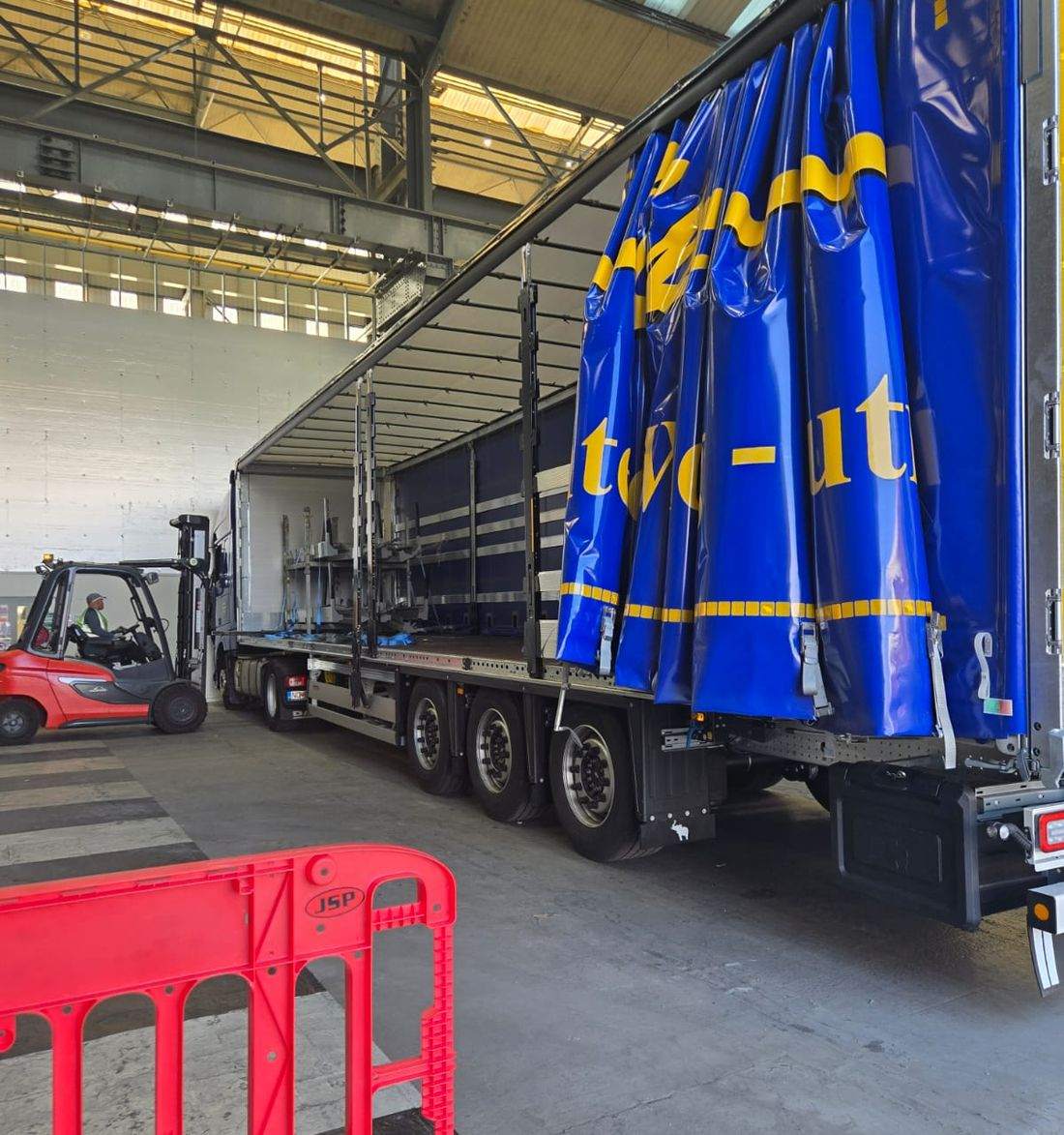 Forklift working a curtainsider with the curtains drawn back, under cover